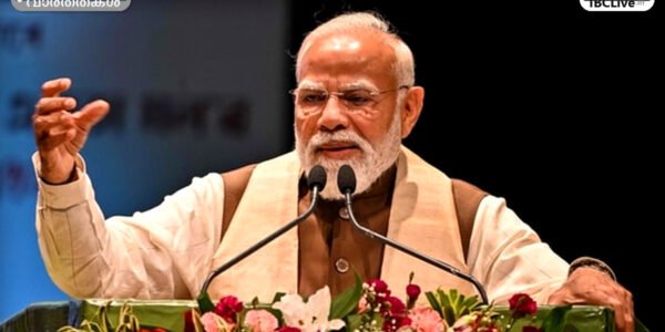 പ്രധാനമന്ത്രി നരേന്ദ്ര മോദി ഒരു മീറ്റിംഗിൽ സംസാരിക്കുന്നു. പശ്ചാത്തലത്തിൽ ഇന്ത്യൻ പതാക കാണാം.