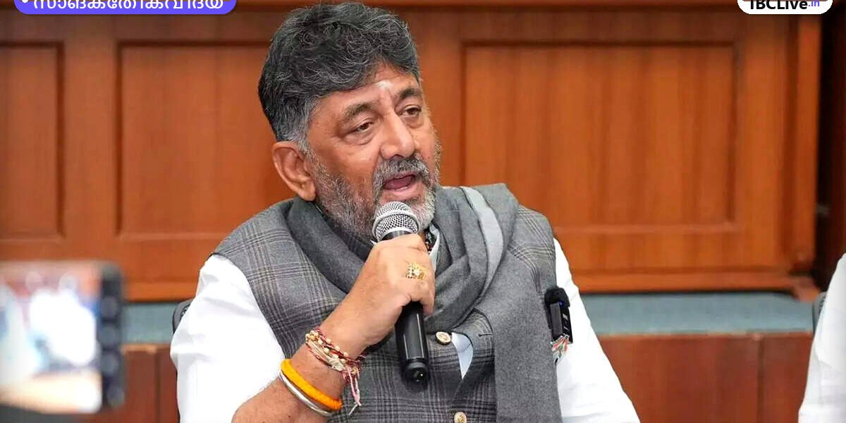 കർണാടക മുഖ്യമന്ത്രി ഡി.കെ. ശിവകുമാർ ഒരു ടെക് കോൺഫറൻസിൽ സംസാരിക്കുന്നു. പിന്നിൽ വലിയ LED സ്ക്രീനിൽ "Future of Tech Karnataka" എന്ന് കാണാം.