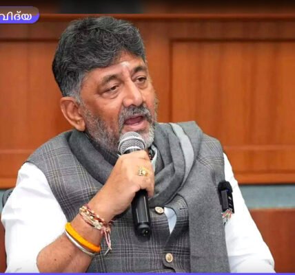 കർണാടക മുഖ്യമന്ത്രി ഡി.കെ. ശിവകുമാർ ഒരു ടെക് കോൺഫറൻസിൽ സംസാരിക്കുന്നു. പിന്നിൽ വലിയ LED സ്ക്രീനിൽ "Future of Tech Karnataka" എന്ന് കാണാം.